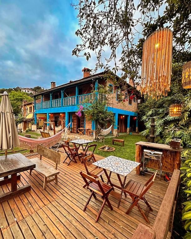 Deck de madeira com mesas, rede e luminárias de franja diante do sobrado azul